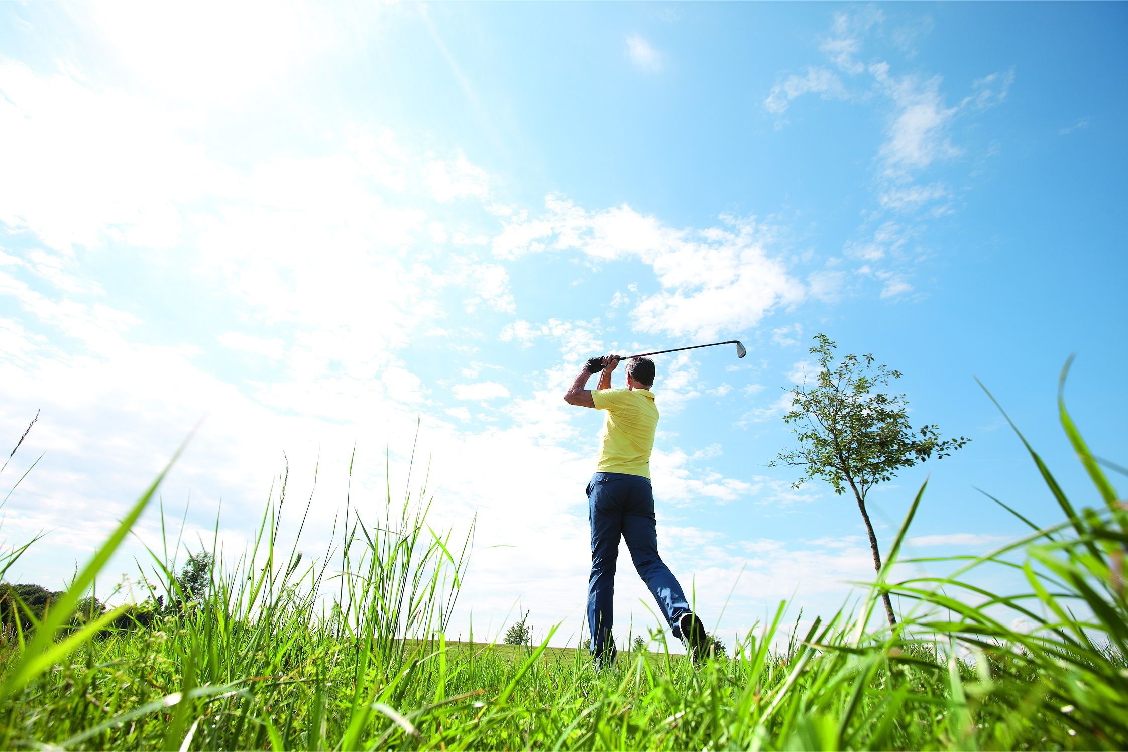 A person playing golf in a grassy field with a clear sky.