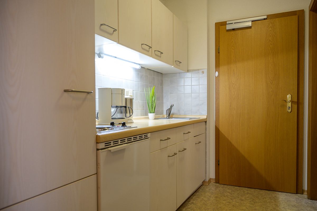 A kitchen with white cabinets, a wooden door, and a countertop with a coffee maker and a potted plant.