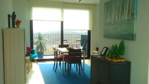 A spacious room with a balcony, a dining area with a table and chairs, a cabinet with a small plant, and a painting of sailboats on the wall. - Fully Equipped Sunny Apartment (Antwerp)