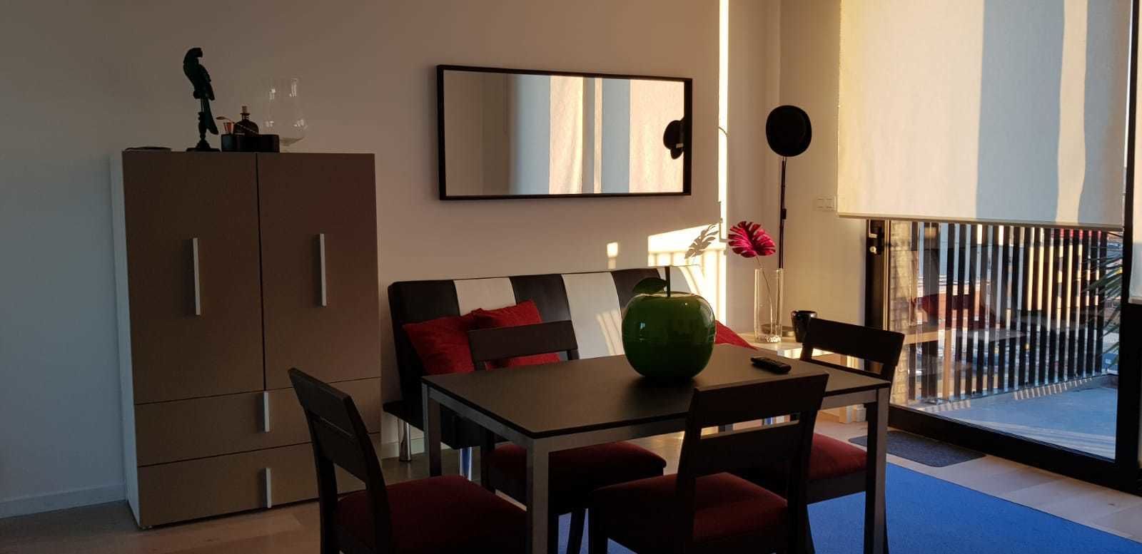 A dining area with a table, chairs, a cabinet, a mirror, and a balcony with a railing.