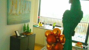A room with a large window, a painting on the wall, a cabinet, and a parrot statue. - Fully Equipped Sunny Apartment (Antwerp)