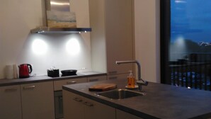 A modern kitchen with a large island, stainless steel appliances, and a view of the city at dusk. - Fully Equipped Sunny Apartment (Antwerp)