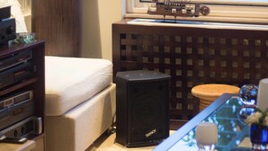 Une chambre avec un lit, un radiateur, une petite table ornée de quelques objets décoratifs, une fenêtre donnant sur la mer et un grand vase rempli de branches.
