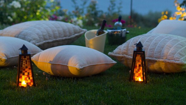 Un cadre extérieur paisible, agrémenté de lanternes et de coussins disposés sur l’herbe, avec vue sur une étendue d’eau calme.