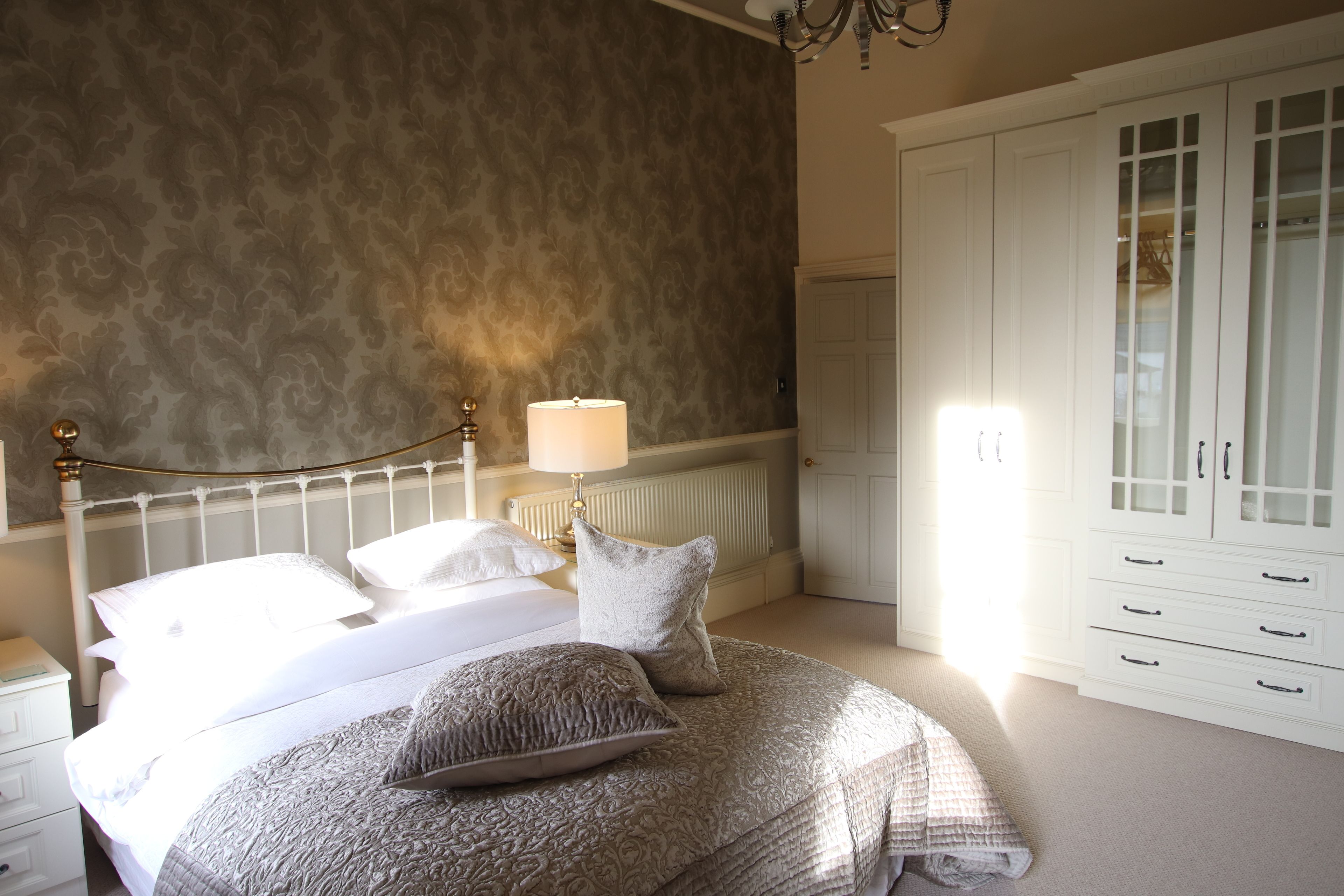 A bedroom with a bed, nightstands, a lamp, a radiator, and a wardrobe.