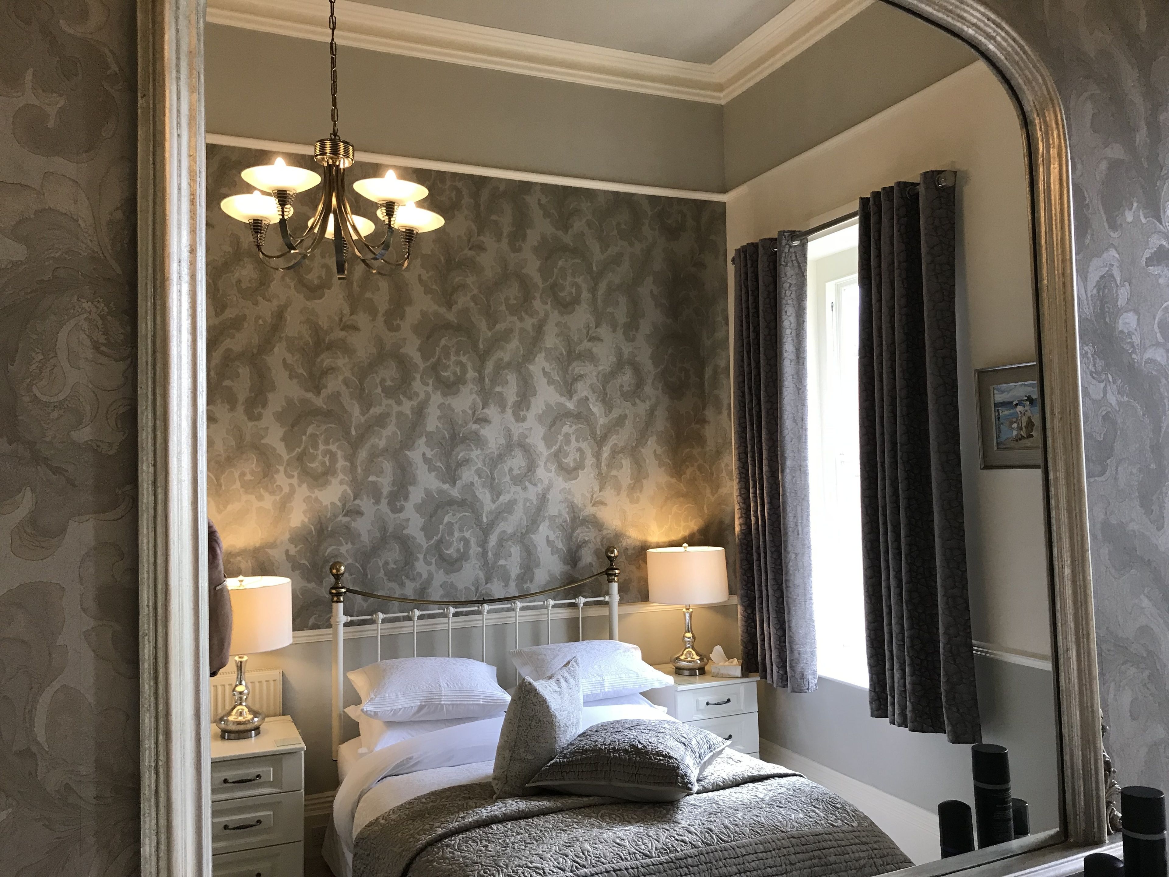 A bedroom with a bed, nightstands, a chandelier, and a large mirror.