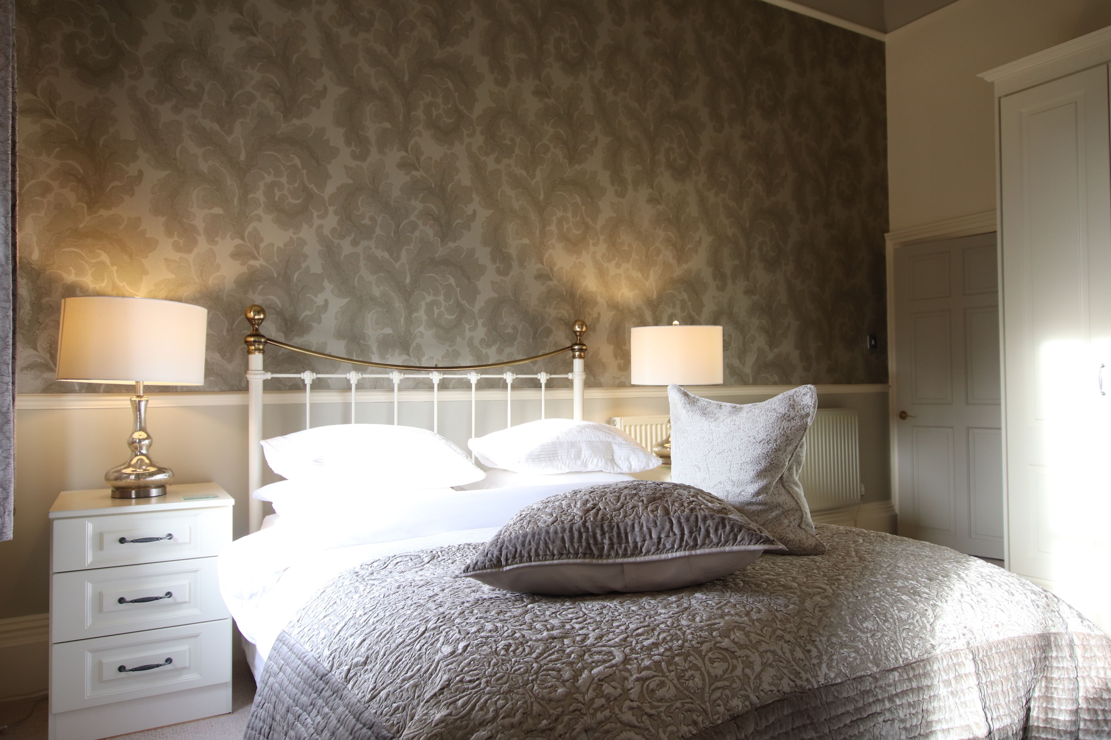 A neatly made bed with a patterned bedspread, two bedside lamps, and a nightstand with drawers.