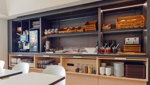 A modern kitchen with built-in appliances, wooden shelves, and a seating area with white chairs. - B&B Hotel Willich (Willich)