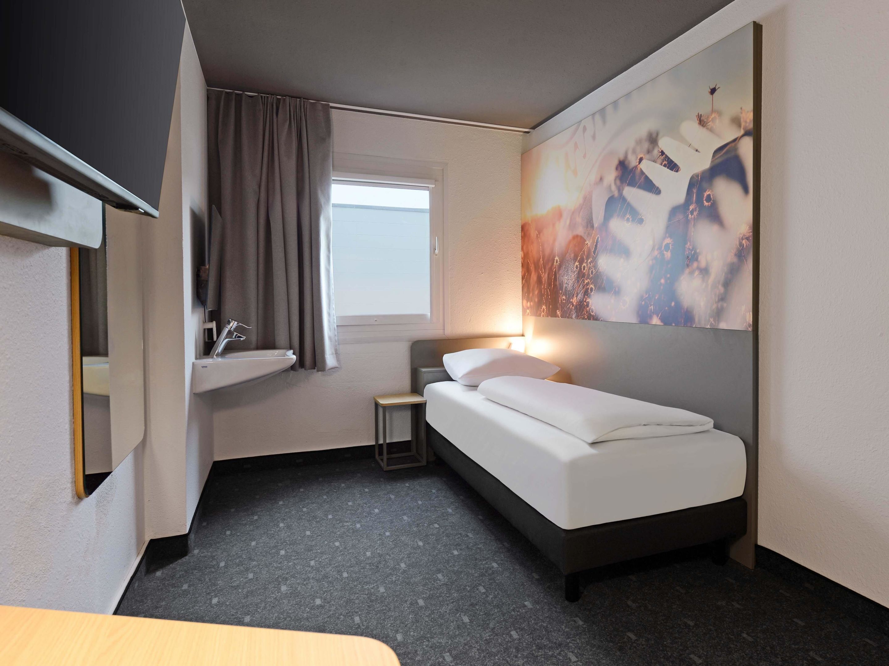 Una habitación de hotel con una cama, una mesita de noche, un lavamanos y una ventana.