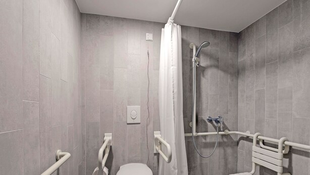 A modern bathroom with a toilet, shower, and grab bars. - B&B Hotel Willich (Willich)
