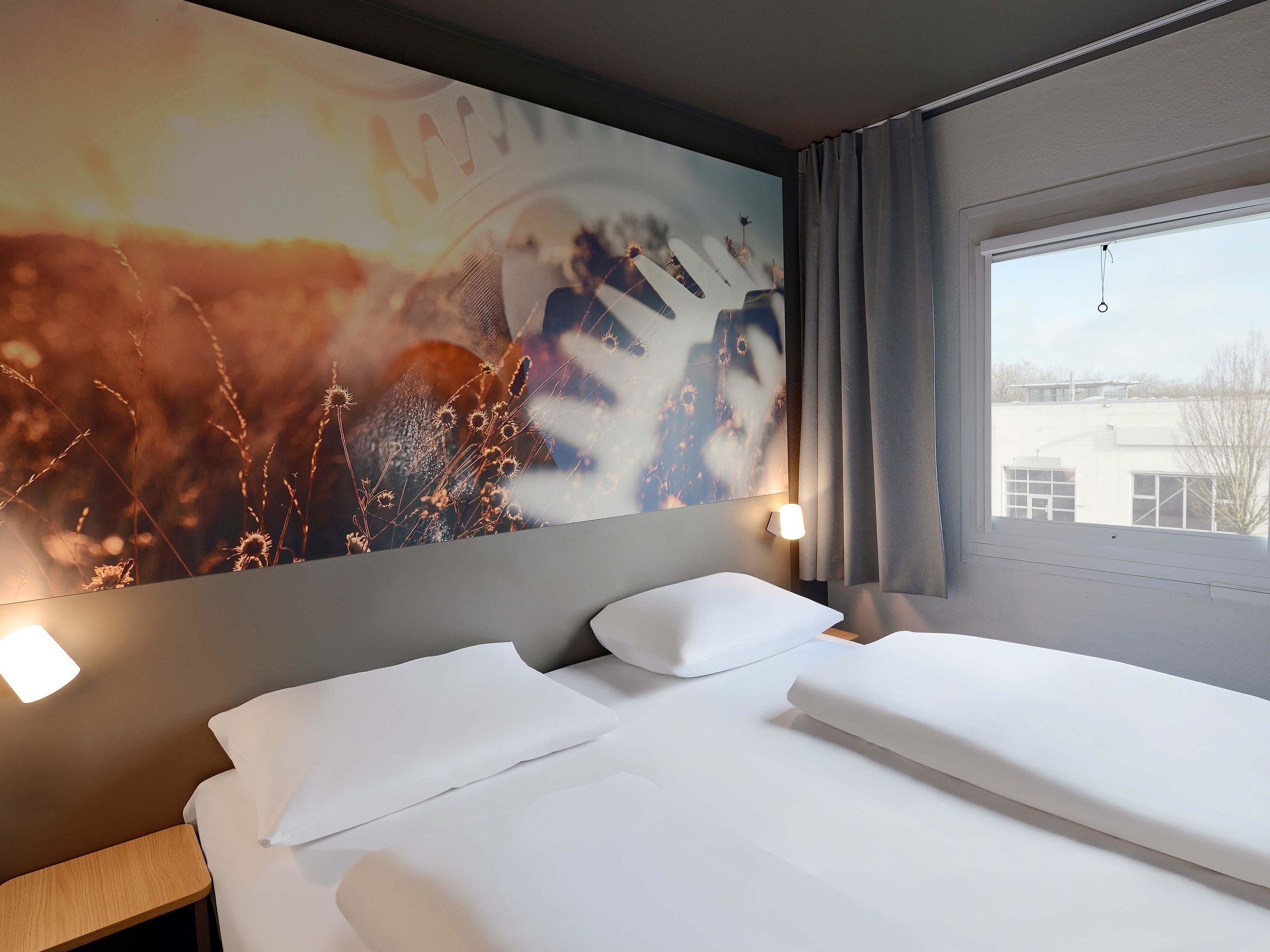 Een hotelkamer met een bed, een nachtkastje, een wandlamp en een raam met gordijnen.