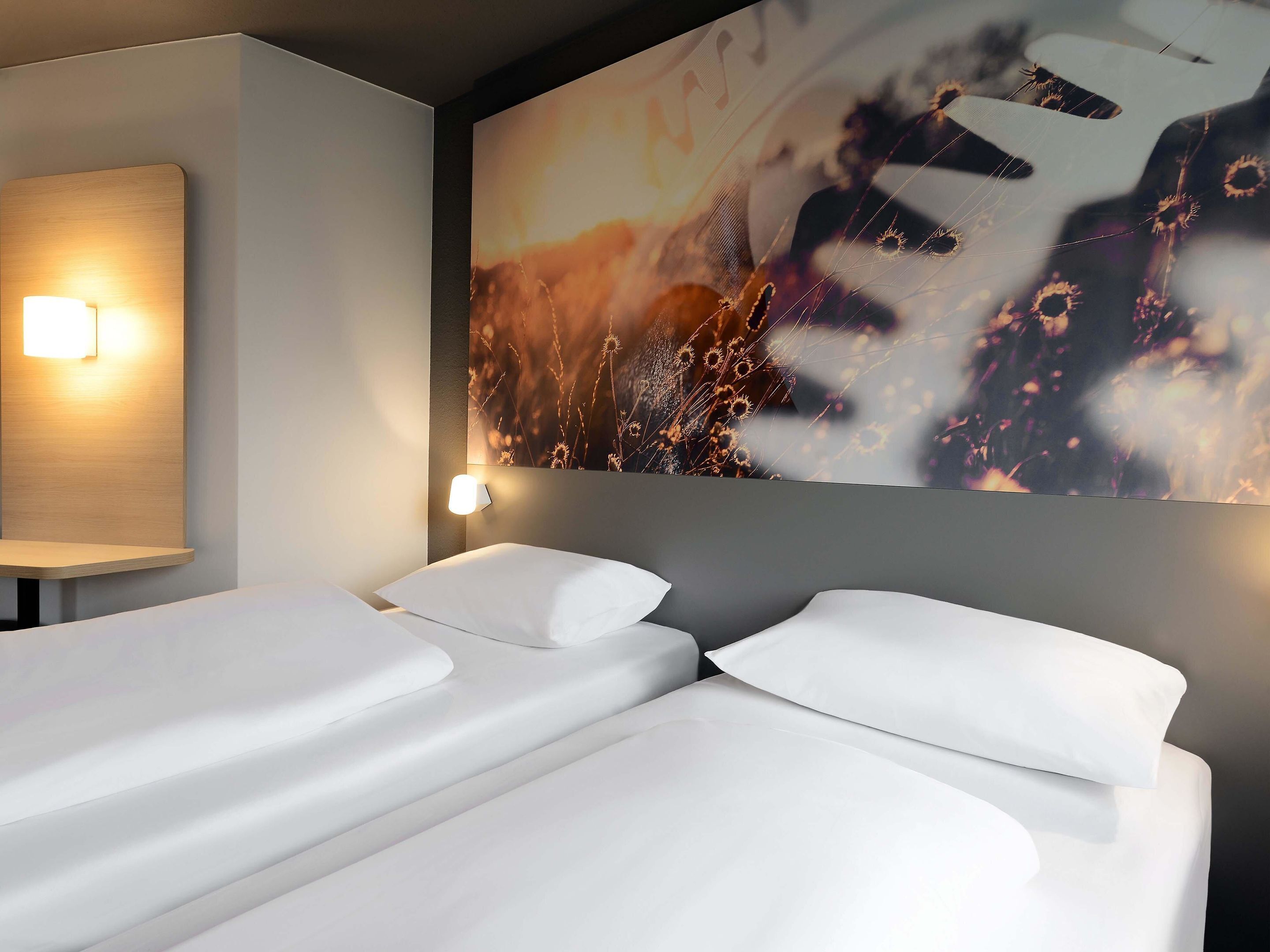 A hotel room with two beds, a wall-mounted light, and a large abstract painting.