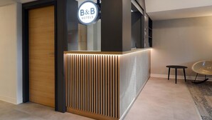 En receptionsdisk med et B&B Hotels skilt, en trædør og et lille rundt bord med en stol.