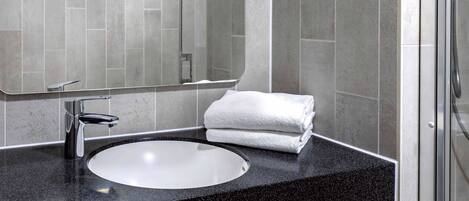 Un baño moderno con encimera de granito negro, lavabo blanco y cabina de ducha de vidrio.