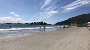 Une plage avec un rivage sablonneux, une eau d’un bleu limpide et une colline qui se dessine à l’horizon.
