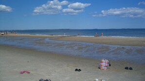 A beach with a blanket and shoes on the sand, and people in the distance. - Sunny Beachfront Cottage with Spectacular Ocean Views  (Saco)