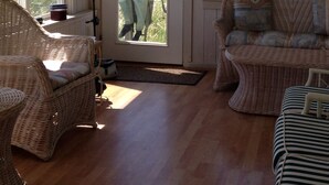 A room with wicker furniture, a door leading outside, and a view of a grassy field. - Sunny Beachfront Cottage with Spectacular Ocean Views  (Saco)