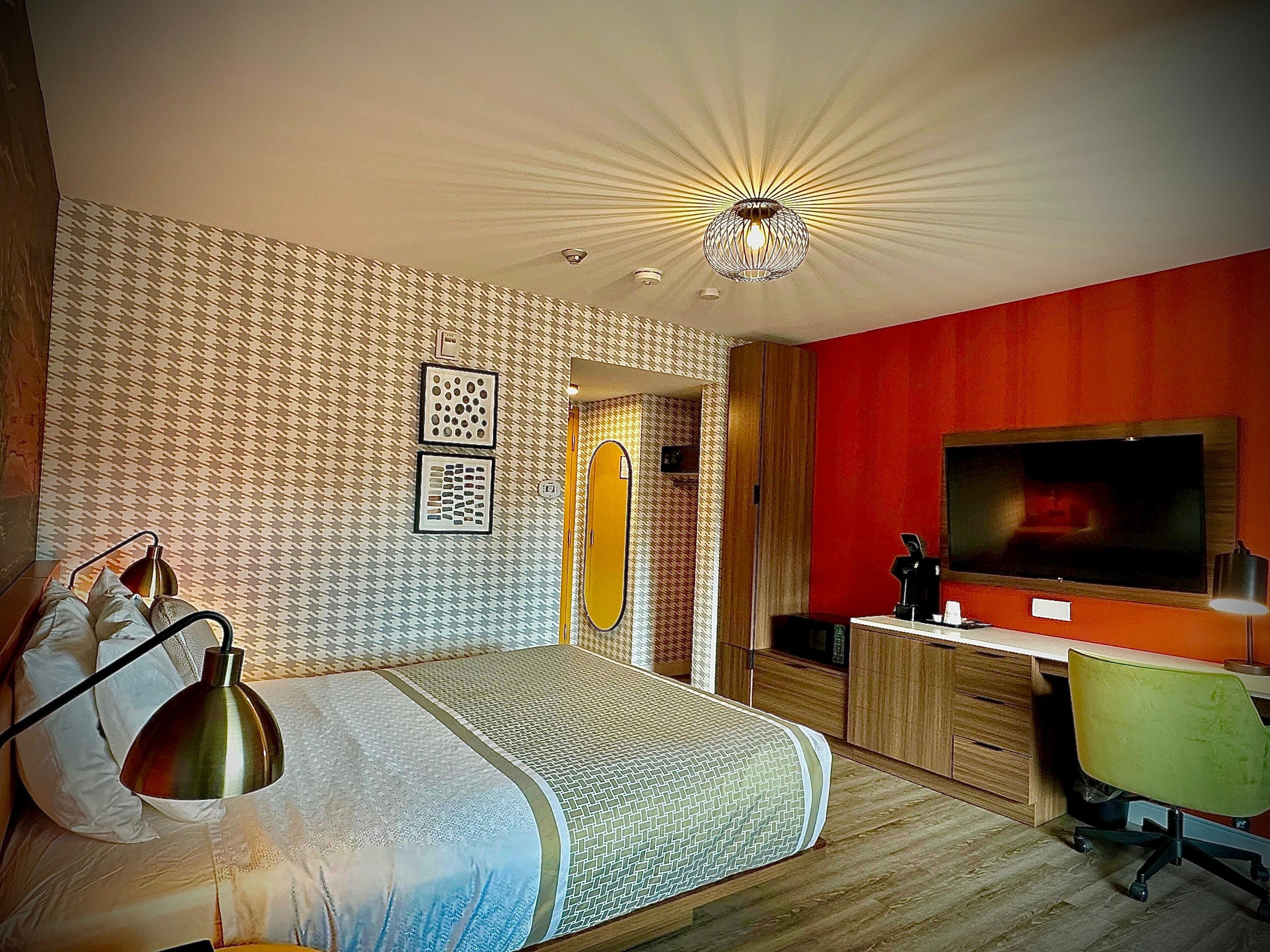 A bedroom with a bed, a desk, a chair, a television, and a ceiling light fixture.
