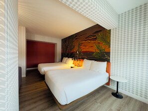 A hotel room with a large bed, a nightstand, a lamp, and a wall mural.
