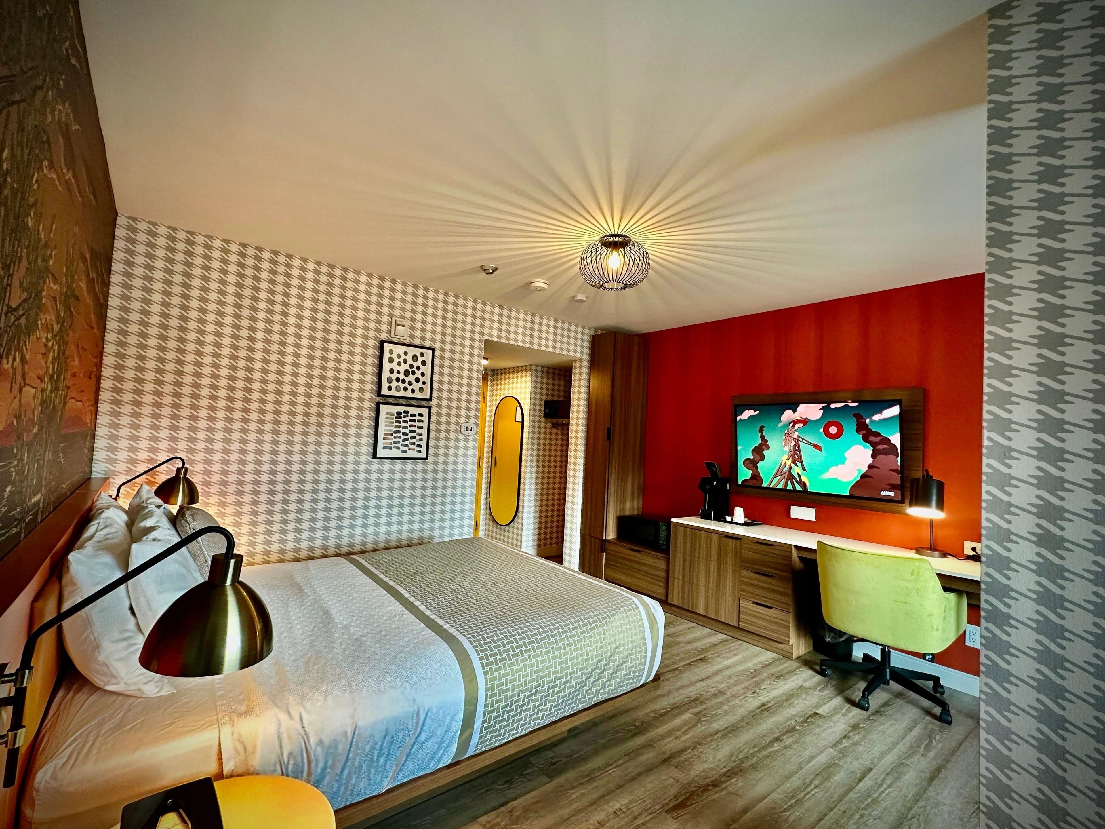 A modern bedroom with a bed, desk, and TV.