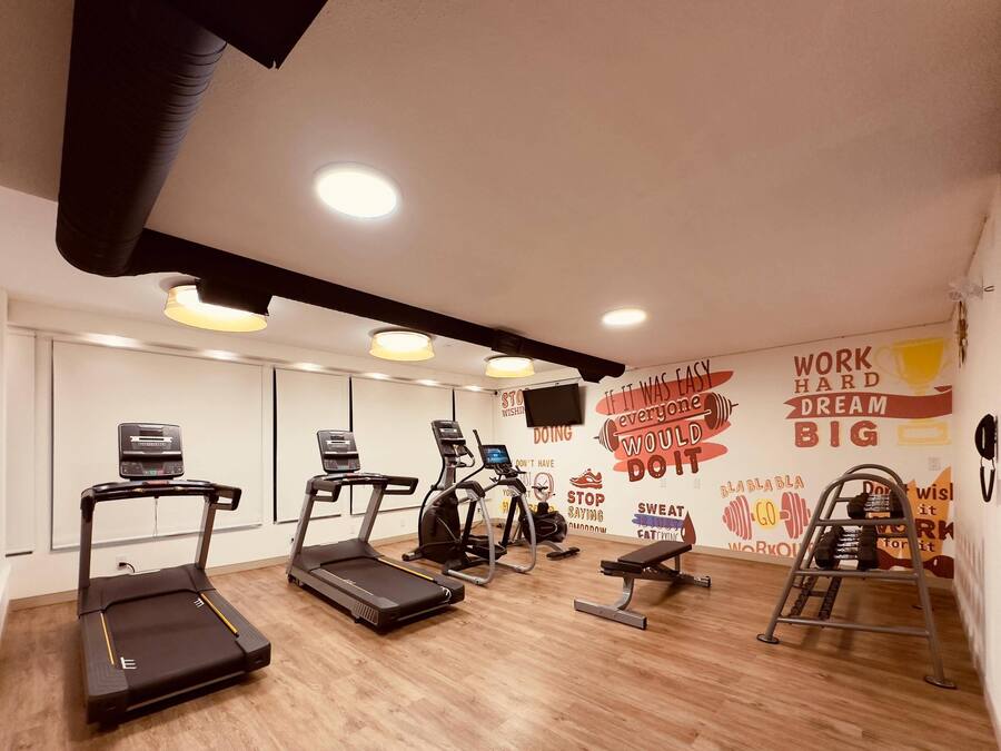 Un gimnasio con cintas de correr, una bicicleta estática, un banco y un soporte para mancuernas.