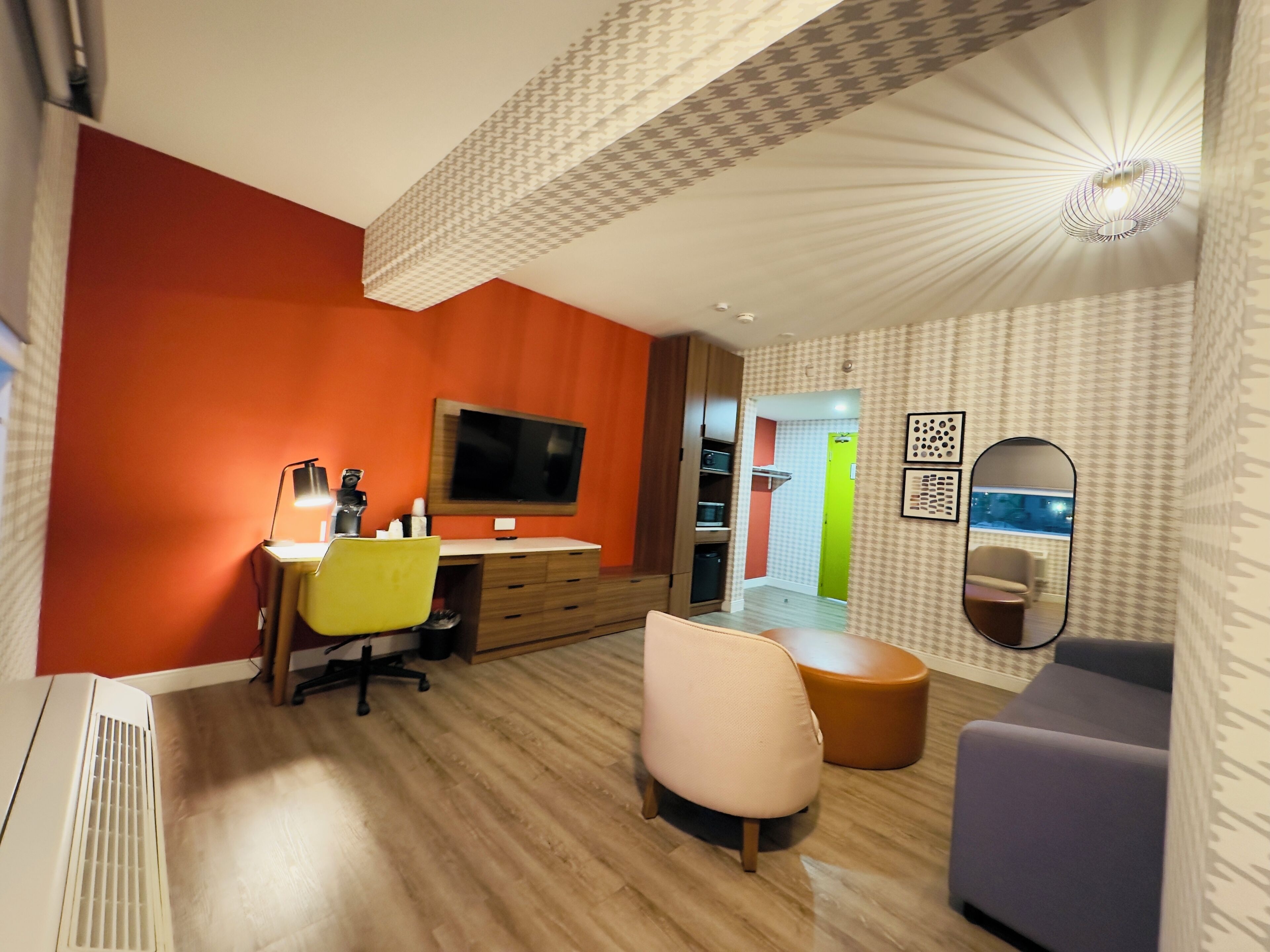 Una sala de estar moderna con una televisión de pantalla plana, un escritorio con una silla, un sofá y un otoman redondos.