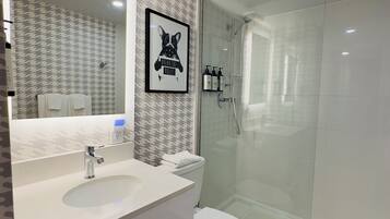 A modern bathroom with a large mirror, a white sink, a toilet, and a glass-enclosed shower.