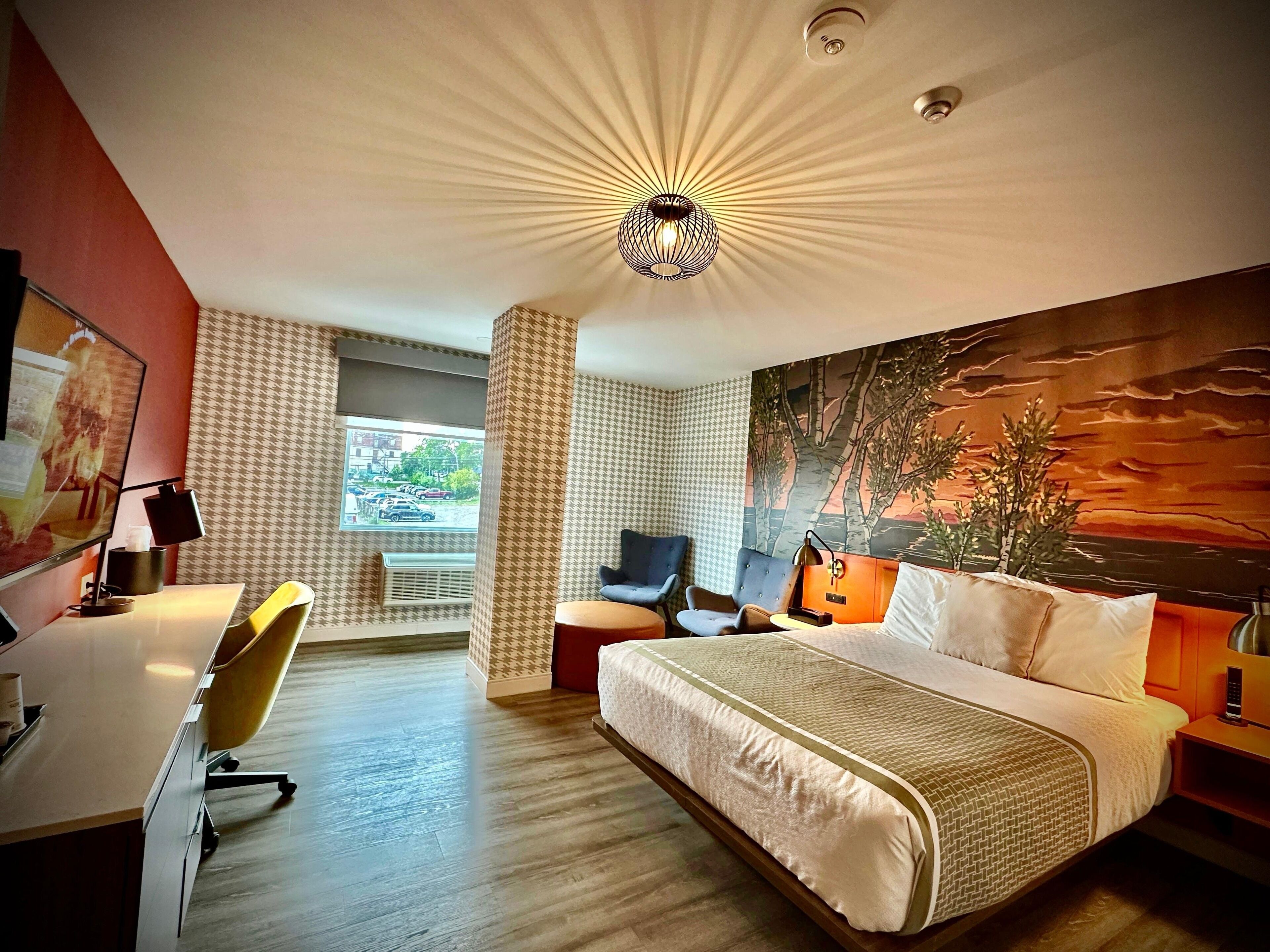 Ett modernt hotellrum med en stor säng, ett skrivbord, en stol och en tavla på väggen.
