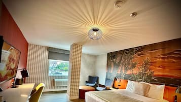 Ett modernt hotellrum med en stor säng, ett skrivbord, en stol och en tavla på väggen.