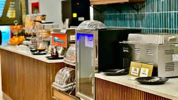A breakfast bar with a coffee machine, a fruit display, and a sign indicating available food items.