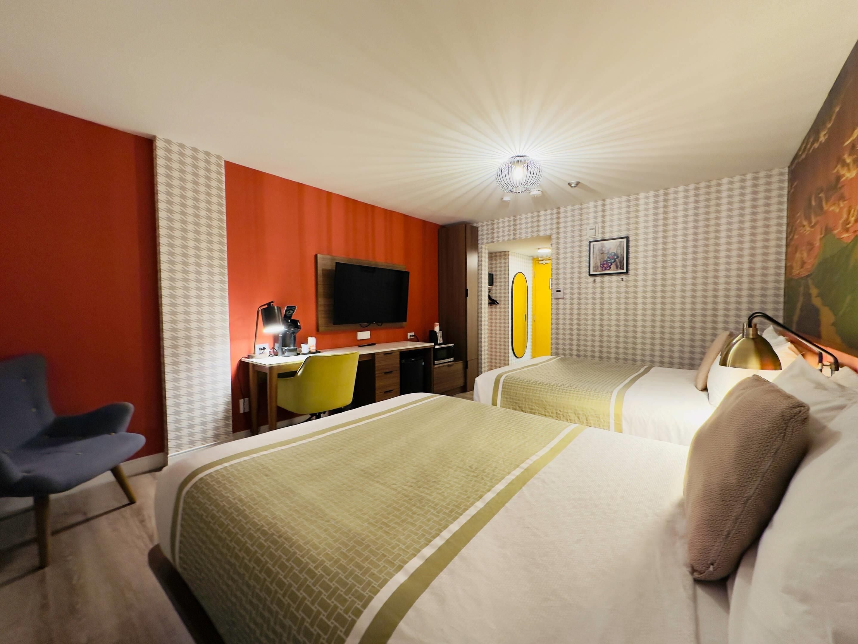 Una habitación de hotel con dos camas, un escritorio con silla, un televisor y un espejo.