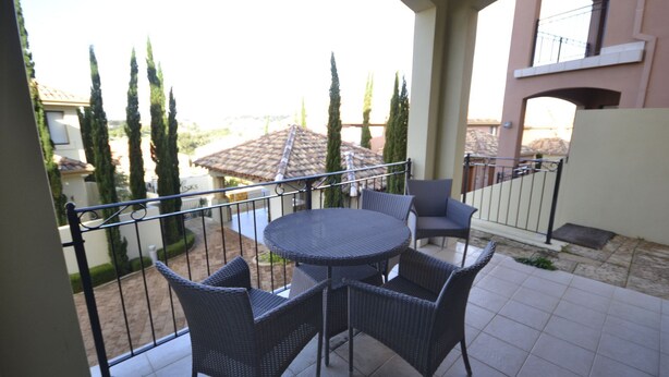 Un balcón con una mesa redonda y cuatro sillas, con vista a un patio con árboles y edificios.