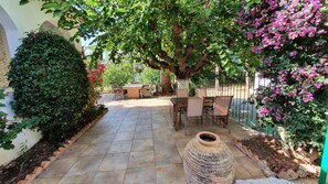 A patio with tiled flooring, outdoor furniture, and a large tree providing shade.