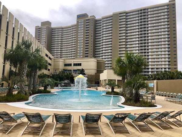 Relax by the resort pool surrounded by palm trees and lounge chairs.