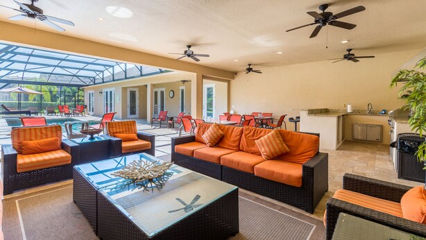 A spacious indoor area with a pool, outdoor seating, ceiling fans, and a kitchen area. - Large outdoor summer kitchen, Private Pool, Theatre Room, 2 miles to Disney ! (Kissimmee)