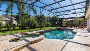 A covered outdoor swimming pool with a patio area, surrounded by palm trees and a view of neighboring houses. - Large outdoor summer kitchen, Private Pool, Theatre Room, 2 miles to Disney ! (Kissimmee)
