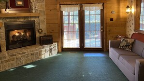 A cozy living room with a stone fireplace, a wooden ceiling fan, and a large window with blinds. - Mtn.View from Hottub, A+ Location 2 Mi to PF.Pkwy,Not up Mtn,Private,SUPERCLEAN (Sevierville)