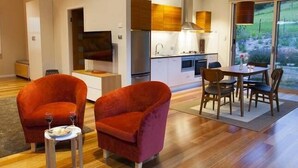 Een moderne woonkamer met een televisie, rode fauteuils, een eettafel met stoelen en een keuken op de achtergrond.