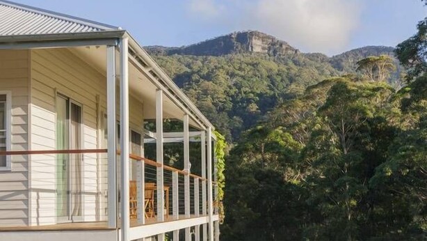 Een huis met balkon, met uitzicht op een bebost dal en een berg.