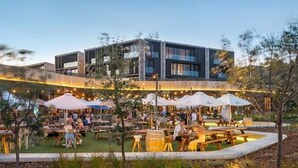 Un espace extérieur aménagé pour les repas, avec des tables et des parasols, un bâtiment moderne en arrière-plan et un jardin bien entretenu.