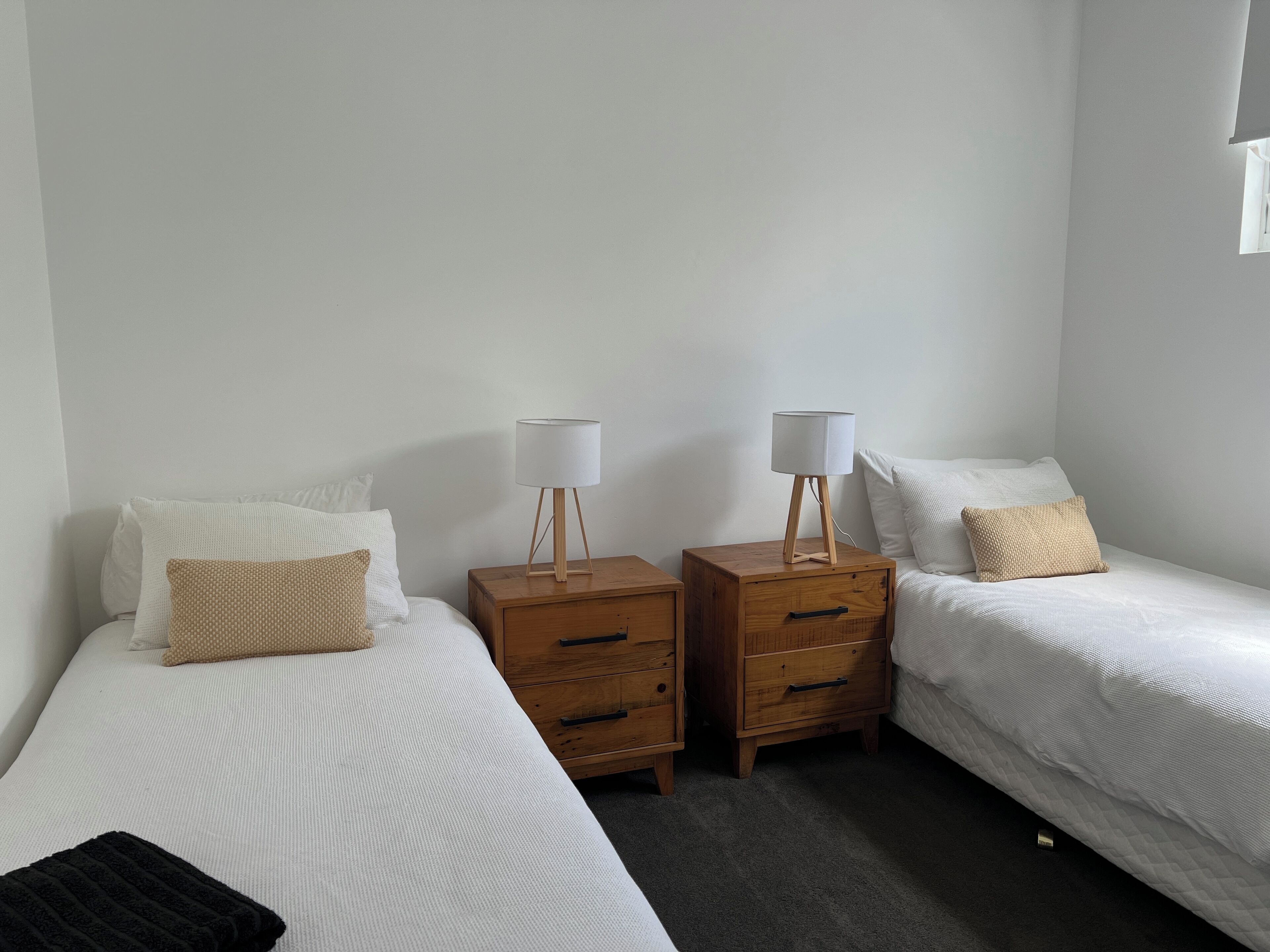 A room with two single beds, each with white bedding and a wooden nightstand with a lamp.
