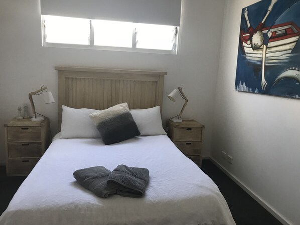 A neatly made bed with a white and gray pillow, two bedside lamps, and a painting of a boat on the wall. - Minutes walk to Beach, Village and Restaurants. Family size home (Freshwater)