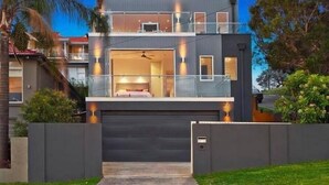 Une maison moderne à deux étages, dotée d’un balcon, de grandes fenêtres et d’un garage.