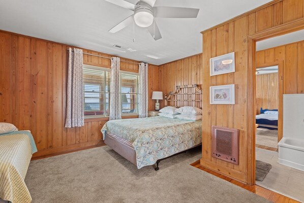 A bedroom with wooden paneling, a bed with patterned bedding, a ceiling fan, and a nightstand with a lamp. - Large Oceanfront Pet Friendly Home perfect for Family Getaways at the Beachcombe (Myrtle Beach)
