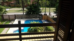 Blick auf einen Pool vom Balkon mit einer Steinsäule und tropischer Bepflanzung.