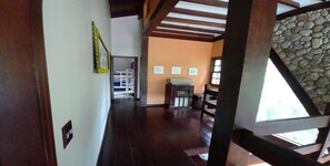 Un pasillo con pared de piedra, vigas de madera y una chimenea. Hay cuadros enmarcados en la pared y una escalera a la derecha.