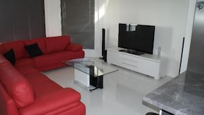 A modern living room with a red sofa, a glass coffee table, a flat-screen TV, and a white entertainment unit.
