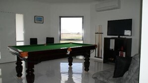 A room with a pool table, a television, and a window with a view.