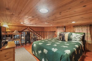Interior de una cabaña de madera con una cama, un escritorio y una escalera.
