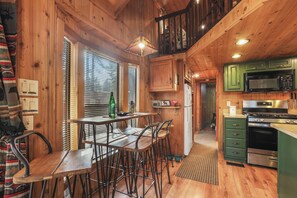 A wooden interior with a kitchen area, including a dining table with chairs, a microwave, and a stove.